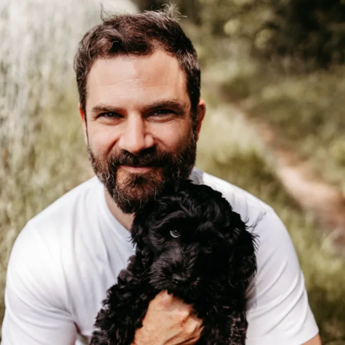 Matthew Perry, smiling, holding a black dog outdoors